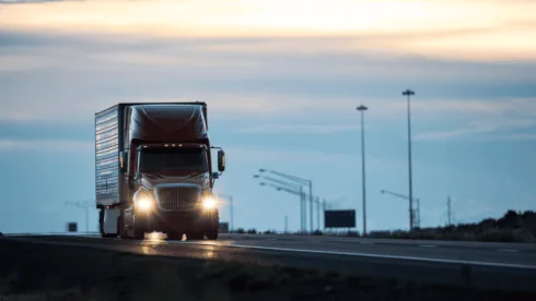 A truck running with its lights on in the evening.
